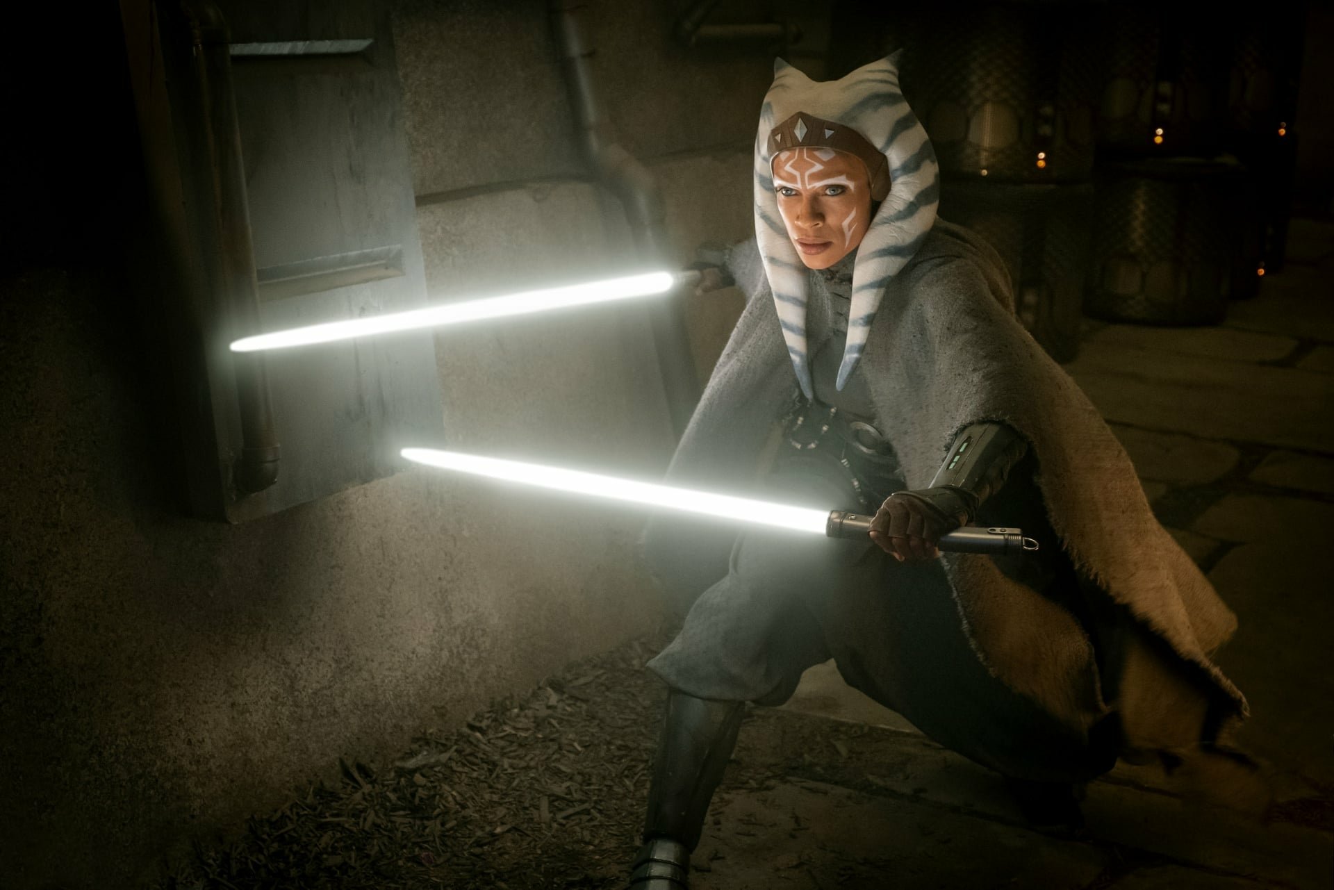 Ahsoka Tano from Star Wars: The Mandalorian, wielding dual white lightsabers in a dim stone corridor — HD PC desktop wallpaper/background.