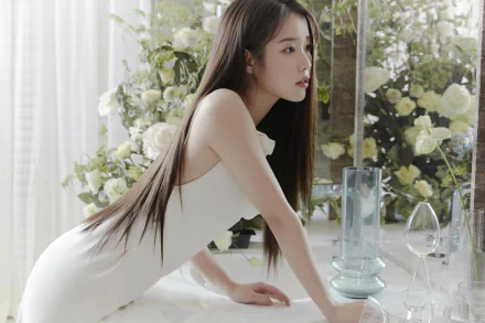 Asian actress and singer Lee Ji-eun in a white dress leans on a marble table, surrounded by flowers and a mirror, captured in 4K Ultra HD.
