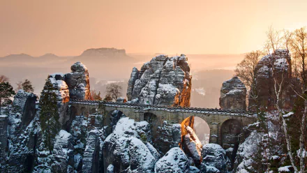 The man-made Bastei Bridge in snow-dusted Elbe Sandstone Mountains, spanning rocky pinnacles at sunrise in Saxony, Germany — 5K UHD desktop wallpaper.