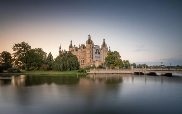 Schwerin Palace — a man-made baroque castle in Germany beside a tranquil lake with a stone bridge; 8K Ultra HD PC desktop wallpaper and background.