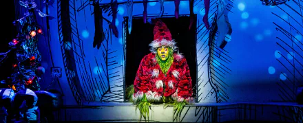 HD wallpaper of The Grinch in red costume peeking out from a snowy window, from Dr. Seuss' The Grinch Musical.