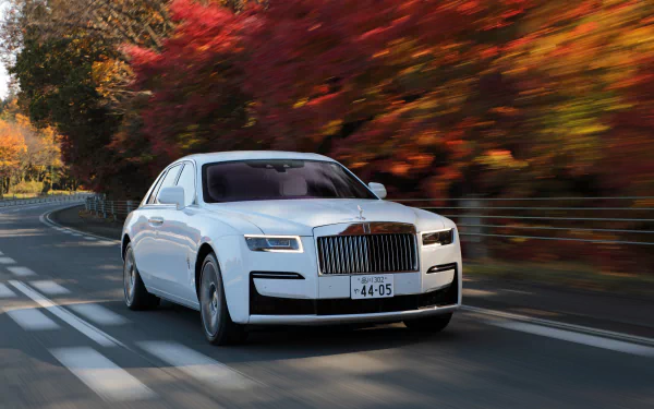 White Rolls-Royce Ghost sedan driving on a winding road amid autumn foliage — 5K Ultra HD PC desktop wallpaper background.