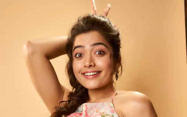 HD desktop wallpaper featuring a playful portrait of Rashmika Mandanna against a warm beige background.