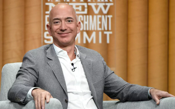 A high-definition desktop wallpaper featuring Jeff Bezos, smiling and seated on a gray armchair at an event, with a backdrop displaying New Establishment Summit.