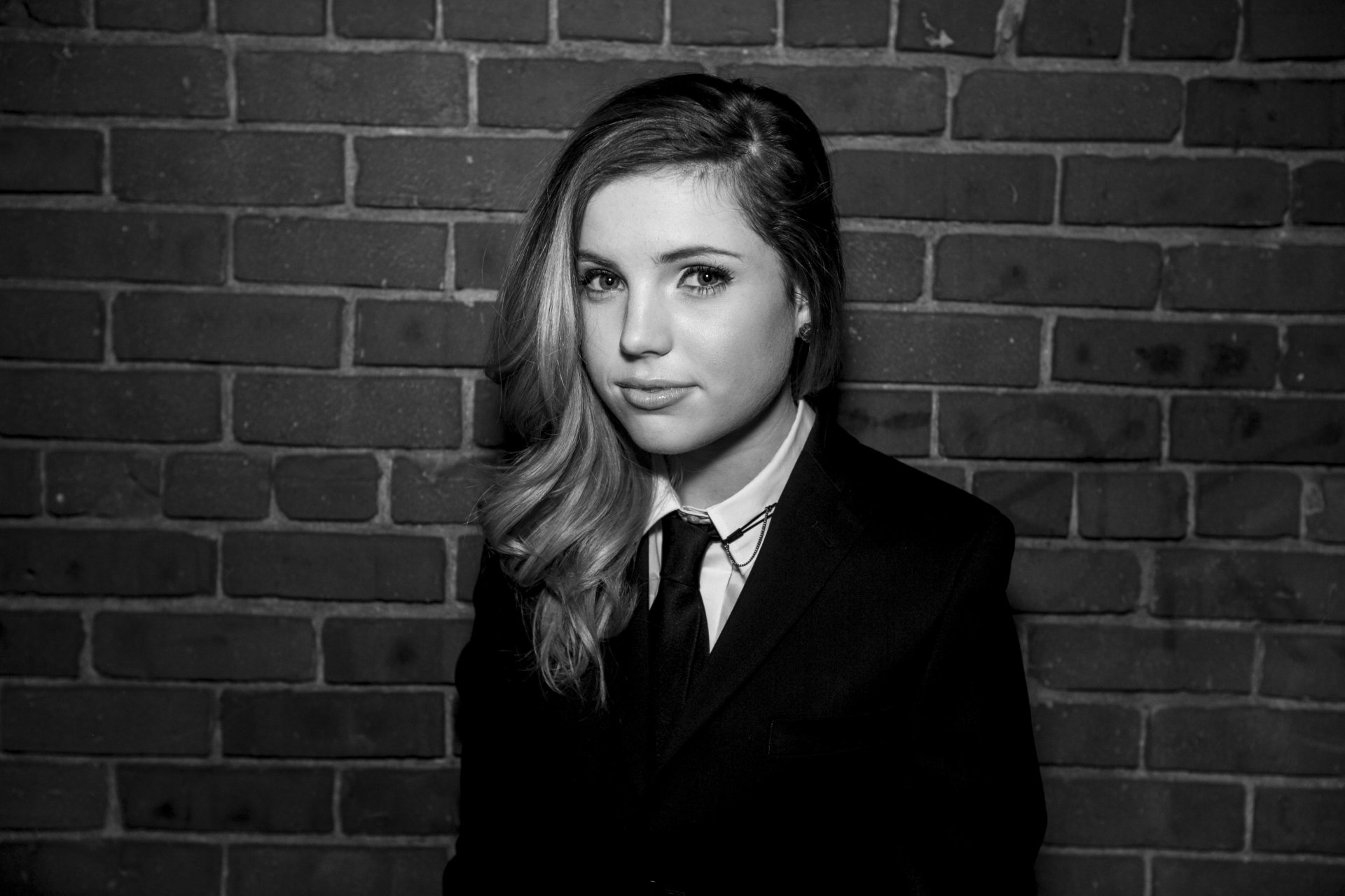 Black and white HD wallpaper featuring a portrait of a woman dressed in a suit against a brick wall background.