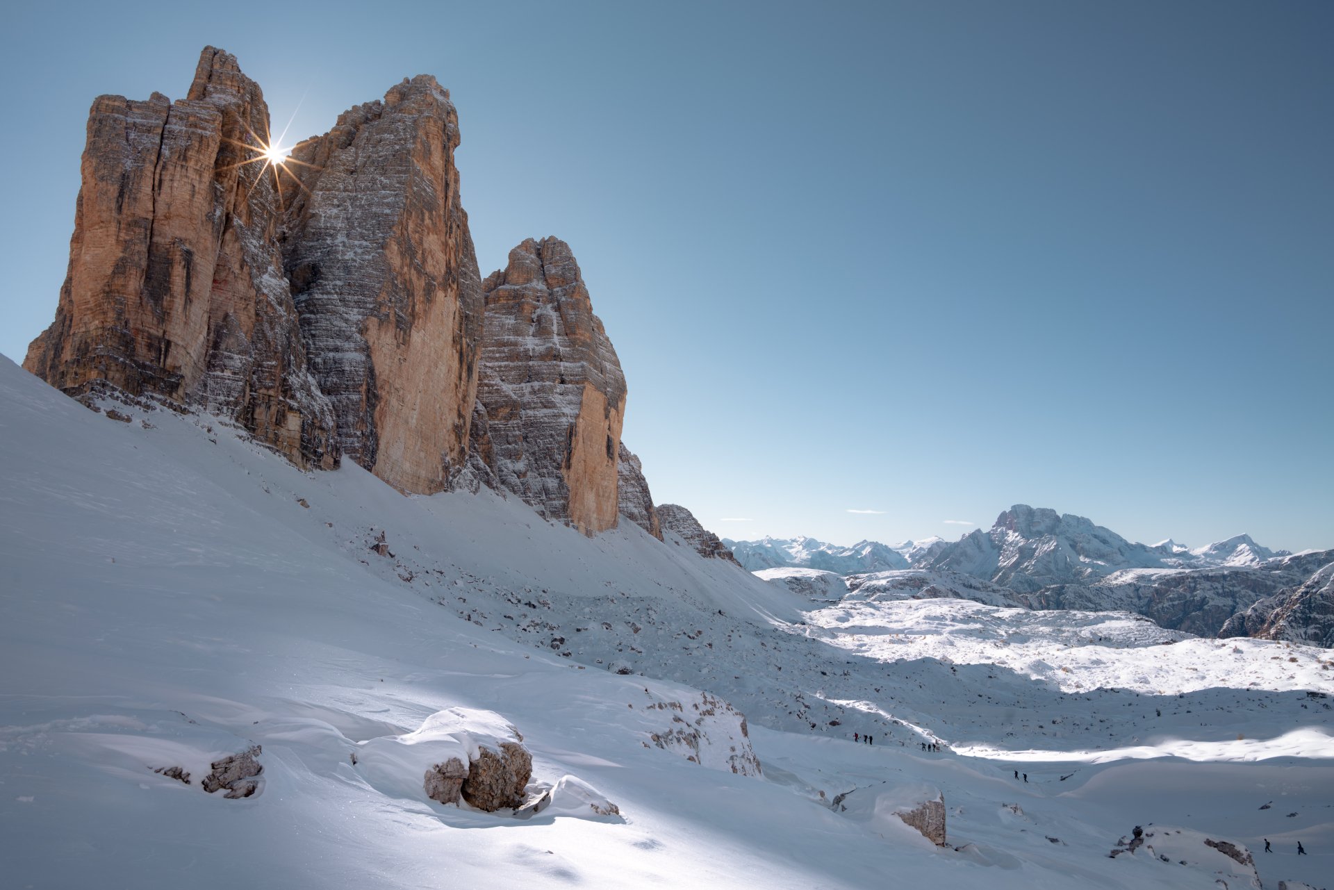Snow-covered Tre Cime di Lavaredo mountain peaks bathed in sunlight under a clear blue sky, captured in stunning 8K Ultra HD nature wallpaper quality.