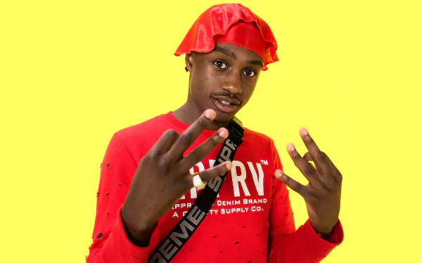 HD desktop wallpaper featuring a person in a red outfit and bucket hat against a yellow background, gesturing with their hands.