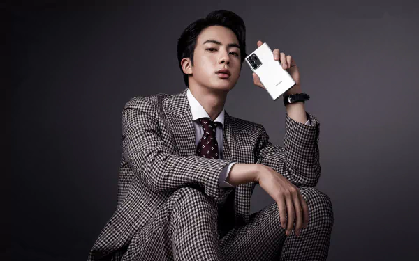Jin (Kim Seokjin) from BTS poses in a checkered suit holding a smartphone, captured in a sharp 4K Ultra HD music-themed desktop wallpaper.
