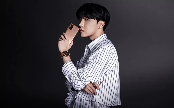 J-Hope (Jung Hoseok) of BTS poses in a striped shirt holding a smartphone, captured in a 4K Ultra HD music-themed PC desktop wallpaper.