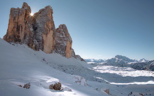 Snow-covered Tre Cime di Lavaredo mountain peaks bathed in sunlight under a clear blue sky, captured in stunning 8K Ultra HD nature wallpaper quality.