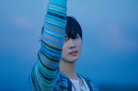 Close-up of a young singer in a striped sweater raising an arm against a soft blue sky — moody K-pop music 4K Ultra HD PC desktop wallpaper and background.