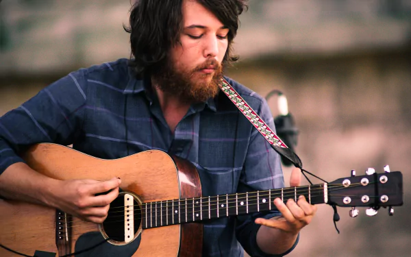 HD desktop wallpaper of a Fleet Foxes member playing an acoustic guitar, evoking a serene musical ambiance.