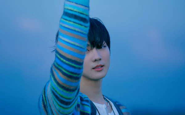 Close-up of a young singer in a striped sweater raising an arm against a soft blue sky — moody K-pop music 4K Ultra HD PC desktop wallpaper and background.