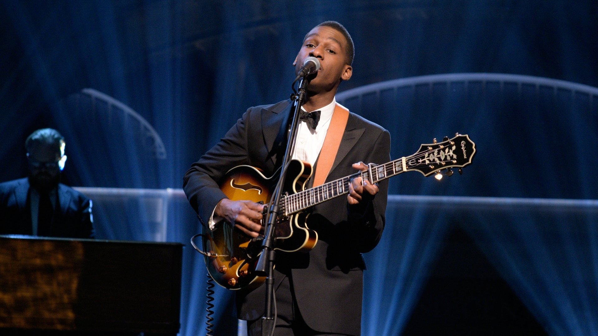 Musician in a suit performs with a guitar on stage, suitable as HD desktop wallpaper and background.