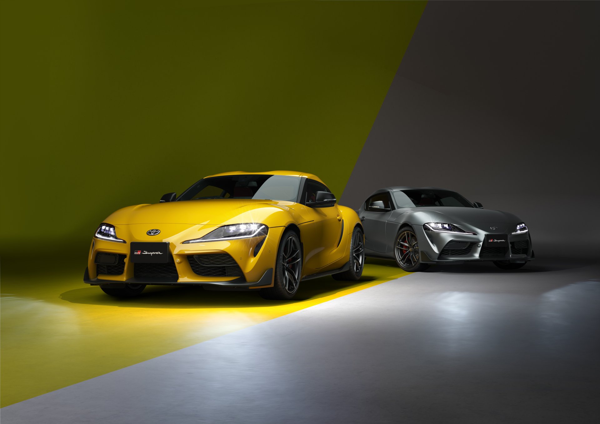 Two Toyota GR Supra vehicles — yellow and silver — dramatically lit against contrasting green and gray backdrops; 5K Ultra HD PC desktop wallpaper/background.
