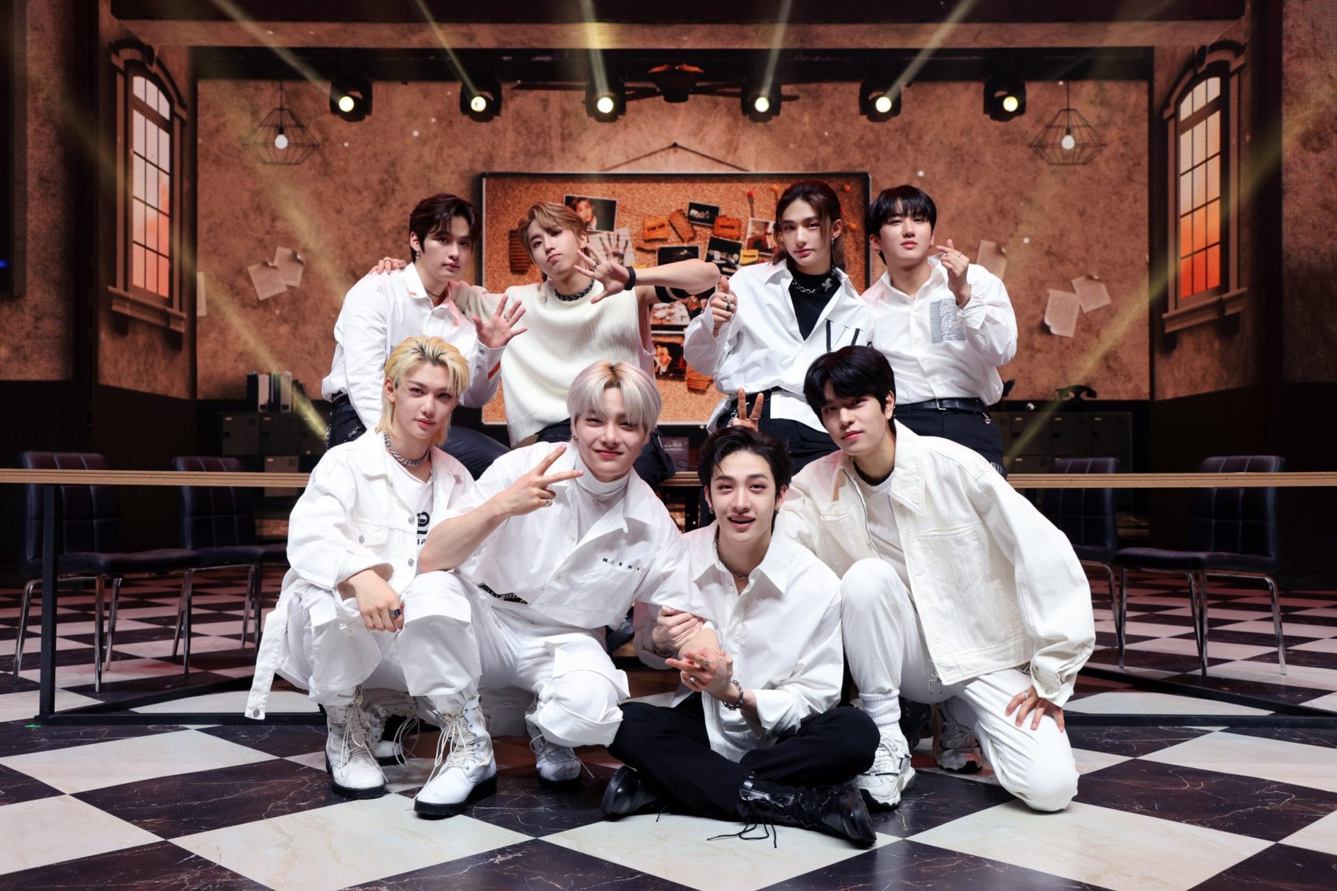 HD PC desktop wallpaper featuring the K-pop boy band Stray Kids posing together in a stylish indoor setting with warm lighting and a checkered floor.