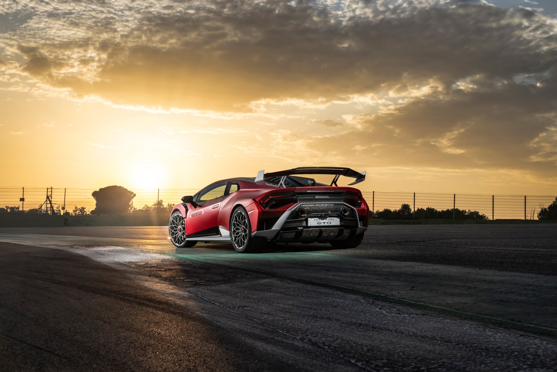 A red Lamborghini Huracán STO supercar parked on a track at sunset, captured in stunning 8K Ultra HD as a PC desktop wallpaper and background.