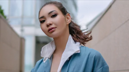HD PC desktop wallpaper: portrait of a woman with pulled-back hair in a teal jacket and white collar, soft urban background.