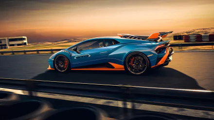 Blue and orange Lamborghini Huracán STO supercar racing along a coastal track at sunset — 4K Ultra HD PC desktop wallpaper and background.