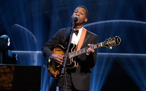 Musician in a suit performs with a guitar on stage, suitable as HD desktop wallpaper and background.