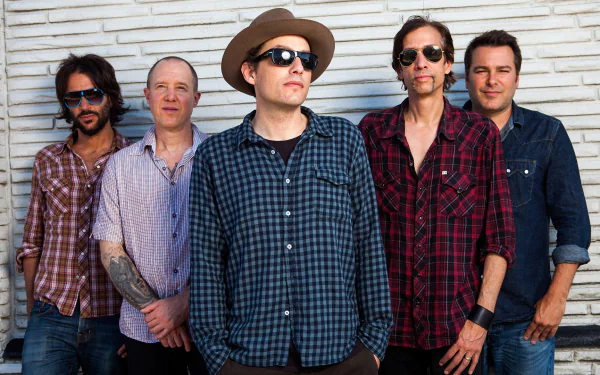 HD desktop wallpaper featuring the band The Wallflowers posing in front of a white brick wall background.