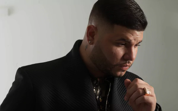 HD wallpaper of a stylish man in a black suit pensively posing for a portrait with a neutral background, tagged as Farruko.