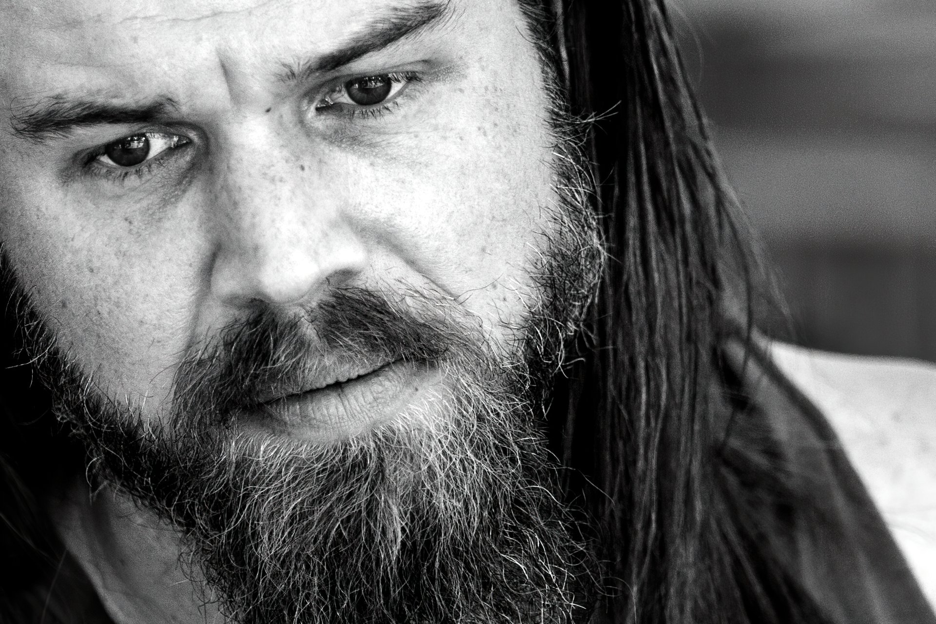 Black-and-white close-up wallpaper of a bearded man with long hair staring intently into the camera.