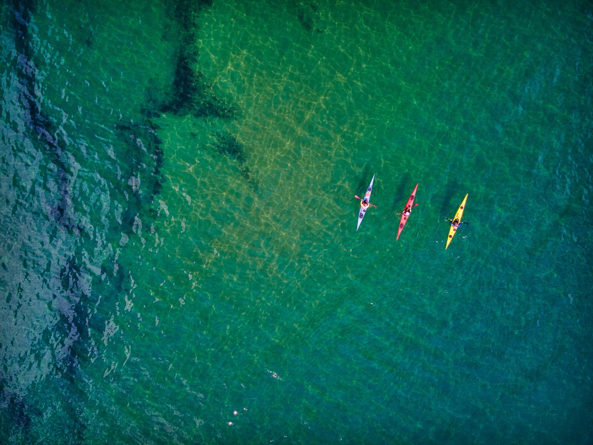 A trio of colourful kayaks navigate the crystal clear shallows along ...