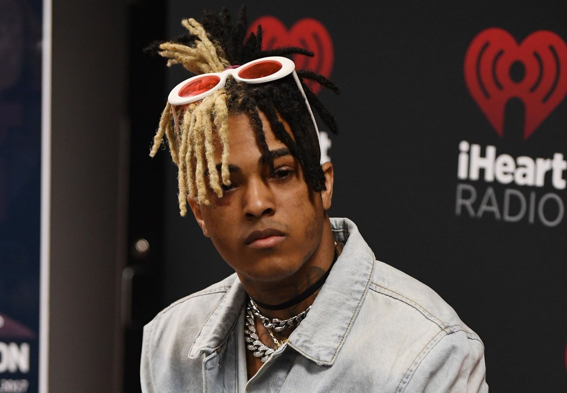 HD PC desktop wallpaper featuring XXXTentacion with his distinctive half-blonde dreadlocks, wearing white sunglasses and a denim jacket at an iHeartRadio event.