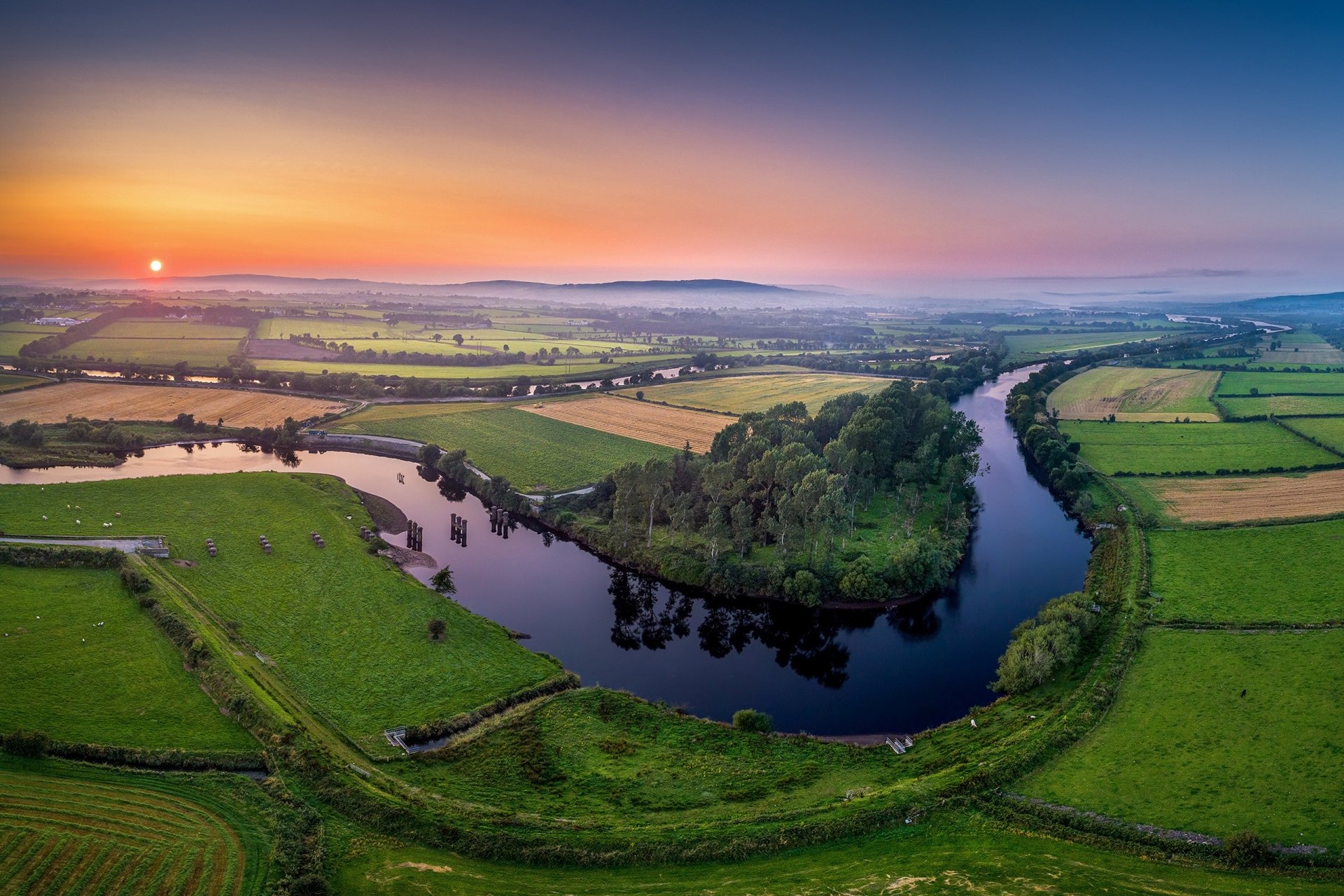 2K Quad HD PC desktop wallpaper: aerial sunrise over an Irish river winding through emerald farmland, lush nature landscape to the horizon.