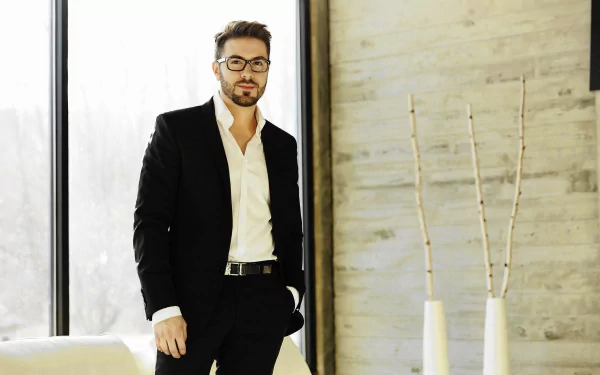 Stylish man in black suit standing in a modern room with natural light, HD desktop wallpaper.