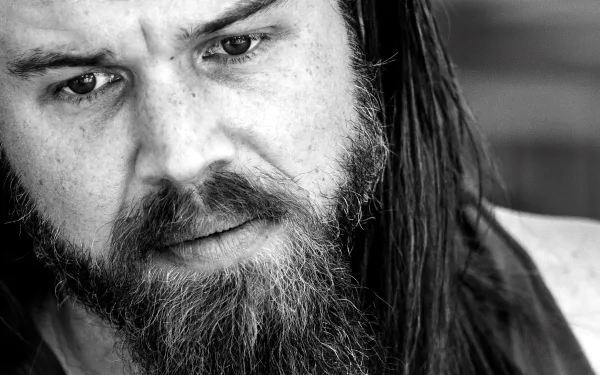 Black-and-white close-up wallpaper of a bearded man with long hair staring intently into the camera.
