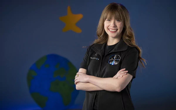A confident woman poses with her arms crossed, wearing an astronaut-themed outfit, against a backdrop featuring a globe and a star, inspired by the Inspiration4 mission.