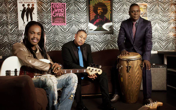HD wallpaper featuring three members of a band posing with their instruments, with a vintage Earth, Wind & Fire album cover in the background.