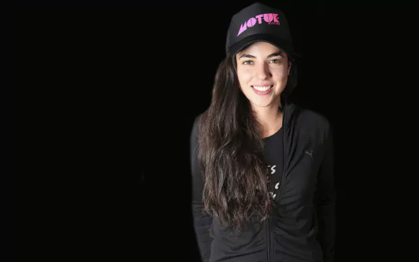 Smiling woman in a black outfit and 'VOTE' cap posing for a HD desktop wallpaper on a dark background.