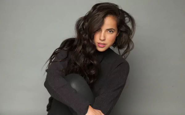 Woman with long hair sitting with crossed arms on a grey background, HD desktop wallpaper.