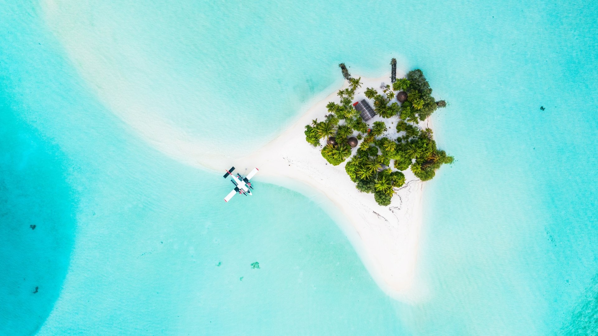 Aerial nature shot of a tiny Maldives island with white sand, turquoise lagoon and a seaplane — 5K Ultra HD PC desktop wallpaper background.
