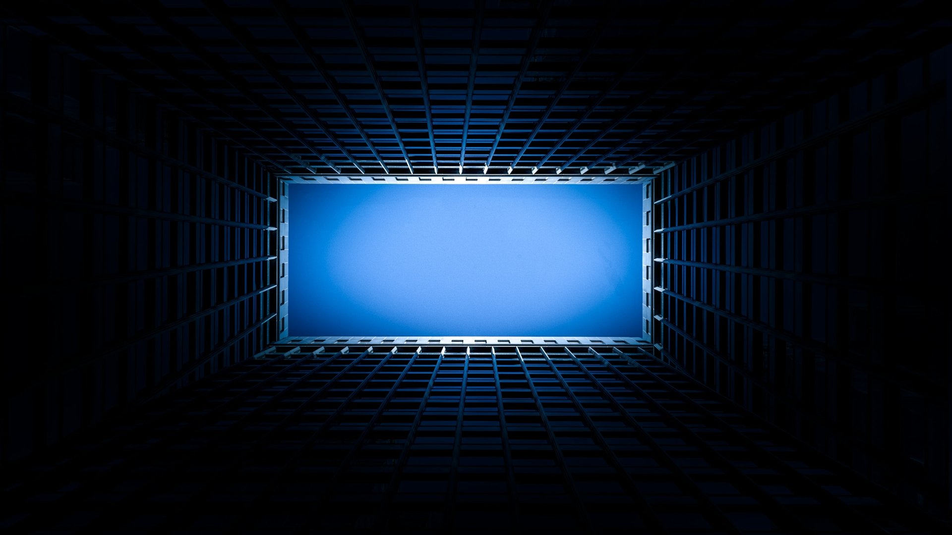 HD wallpaper showing the interior of a building skylight, featuring a symmetrical grid pattern and a bright blue sky above.