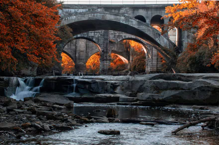 A 4K Ultra HD desktop wallpaper of a stone bridge over a waterfall in Ohio, surrounded by vibrant autumn trees and flowing water.