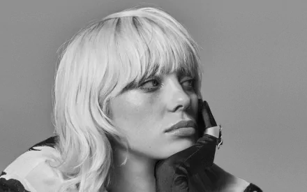 Black and white 4K Ultra HD wallpaper featuring a close-up of Billie Eilish with platinum blonde hair, resting her face on a gloved hand against a plain background.