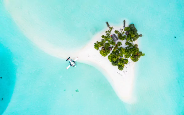 Aerial nature shot of a tiny Maldives island with white sand, turquoise lagoon and a seaplane — 5K Ultra HD PC desktop wallpaper background.