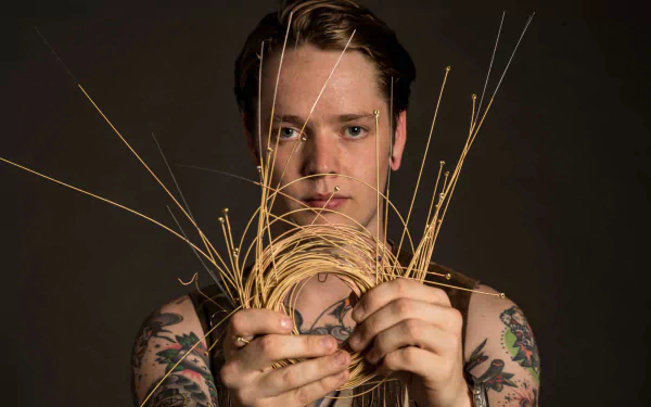 HD desktop wallpaper featuring a person holding strings with tattoos on arms against a dark background.