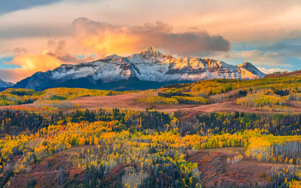 4K Ultra HD desktop wallpaper showcasing a vibrant fall landscape with colorful foliage and a majestic mountain range under a glowing sky.