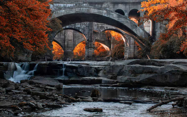 A 4K Ultra HD desktop wallpaper of a stone bridge over a waterfall in Ohio, surrounded by vibrant autumn trees and flowing water.