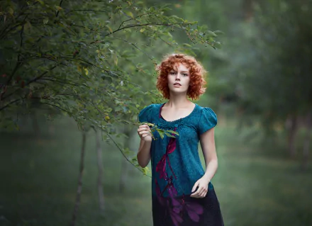 HD desktop wallpaper showing a redhead woman model in a teal dress standing amid lush green trees in a serene outdoor setting.
