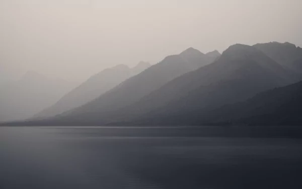 Misty silhouettes of mountain ridges over a calm lake in Grand Teton National Park, captured in stunning detail for an 8K Ultra HD desktop wallpaper.