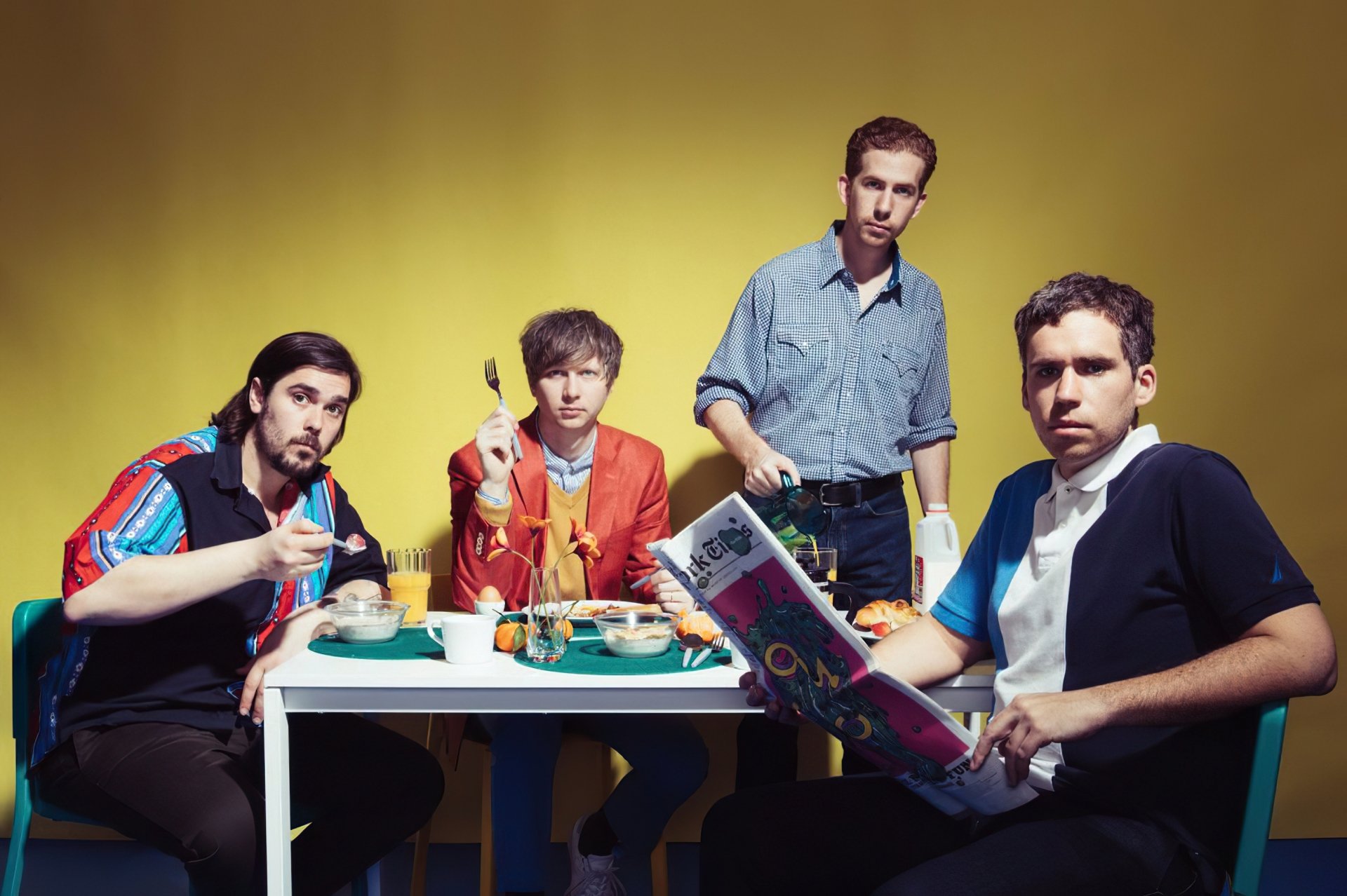 HD desktop wallpaper featuring four members of the band Parquet Courts sitting at a table against a yellow background.