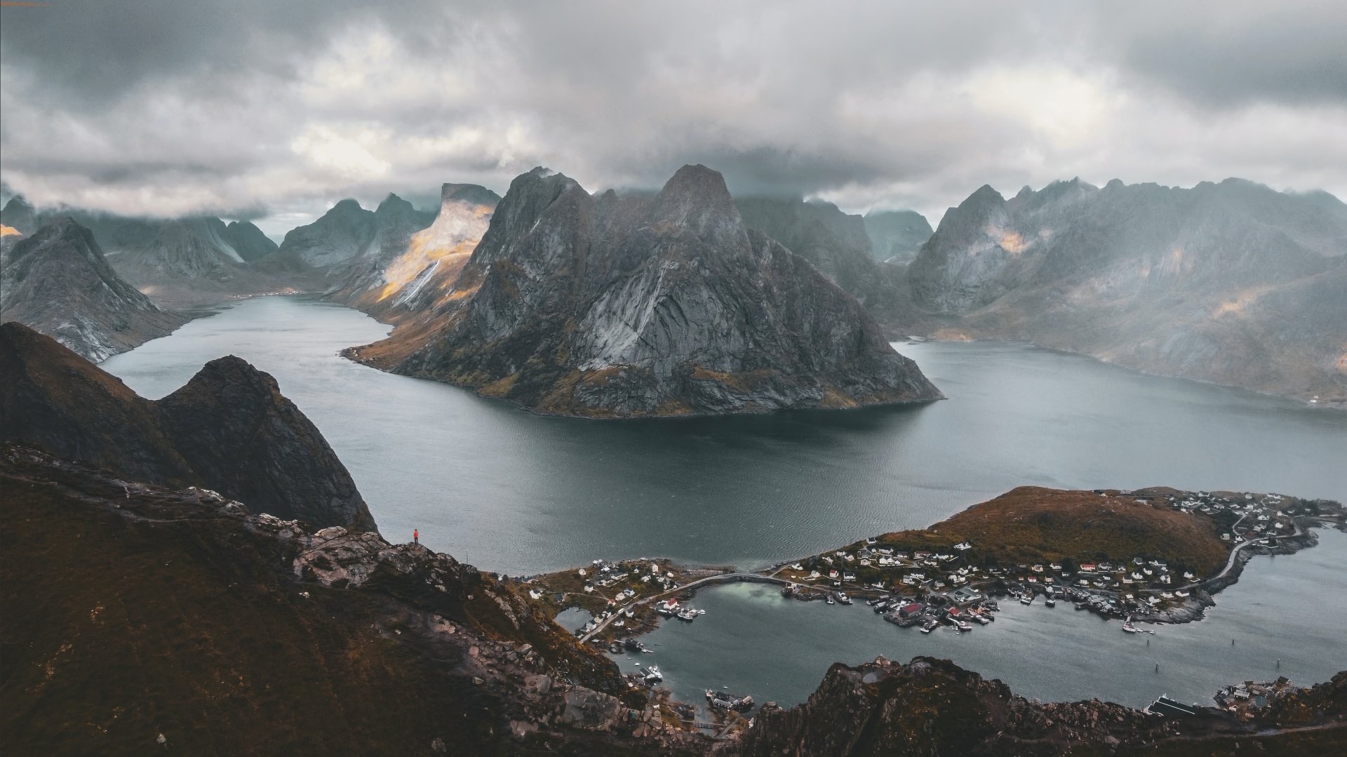 4K Ultra HD photography of Lofoten: dramatic fjords and jagged peaks above a coastal village, moody clouds — PC desktop wallpaper and background.