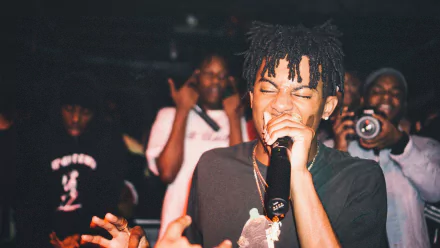 A vibrant HD wallpaper featuring Playboi Carti passionately performing on stage, surrounded by an engaged audience. The energetic atmosphere captures the essence of live music.
