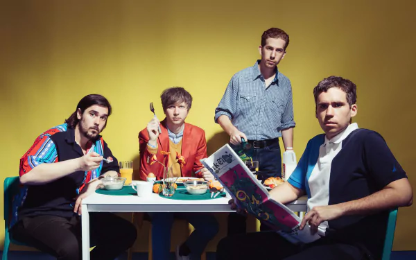 HD desktop wallpaper featuring four members of the band Parquet Courts sitting at a table against a yellow background.